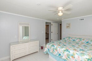 Ein Schlafzimmer mit Bett, Kommode, Spiegel, Deckenventilator und einer Tür zu einem anderen Raum.