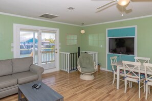 A living room with a sofa, a coffee table, a TV, a ceiling fan, and a view through the door. - A Leave of Absence - 5BR Canalfront Home with Covered Porches and Boat Dock (Topsail Beach)