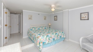 A bedroom with a bed, a ceiling fan, a door, and wall-mounted artwork.