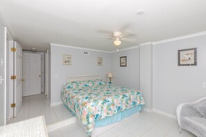 A bedroom with a bed, a ceiling fan, a door, and wall-mounted artwork.
