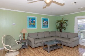 A living room with a sectional sofa, a small side table, a lamp, and two framed paintings on the wall. - A Leave of Absence - 5BR Canalfront Home with Covered Porches and Boat Dock (Topsail Beach)