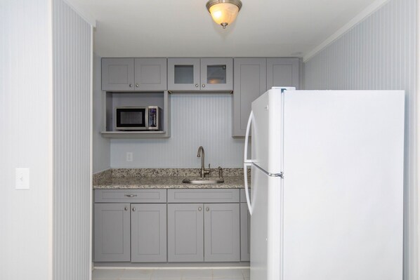 Una cocina compacta con microondas integrado, un lavamanos y un refrigerador blanco.