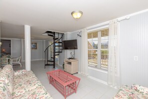 Ein Wohnzimmer mit einer Couch, einem rosafarbenen Tisch, einem Fernseher und einer Wendeltreppe.