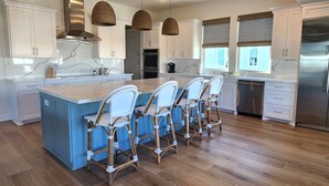 A modern kitchen with a central island, bar stools, and stainless steel appliances. - Ultimate Beach Escape -4BR Luxury with EV Charging (Galveston)