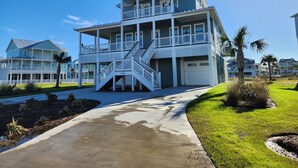 A multi-story beachfront house with a covered porch, a garage, and a well-maintained lawn. - Ultimate Beach Escape -4BR Luxury with EV Charging (Galveston)