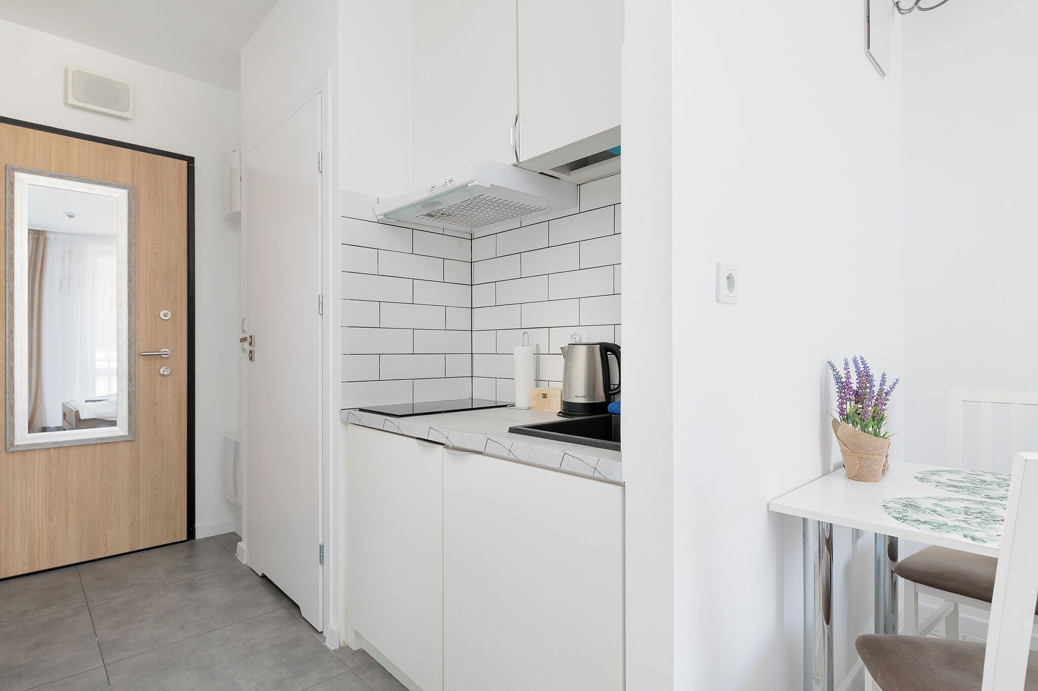 A modern kitchen with white cabinets, a black countertop, and a stainless steel kettle.