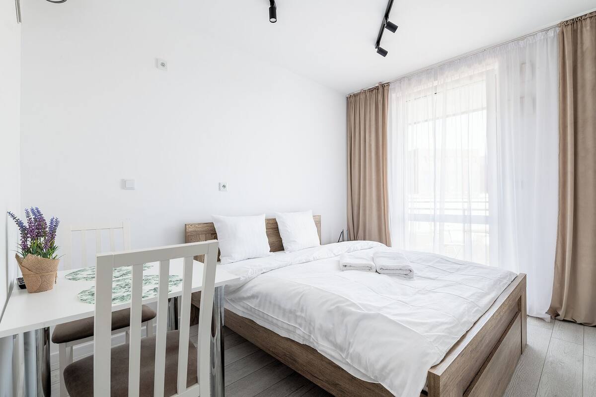 A bedroom with a bed, a bedside table, a chair, and a window with curtains.