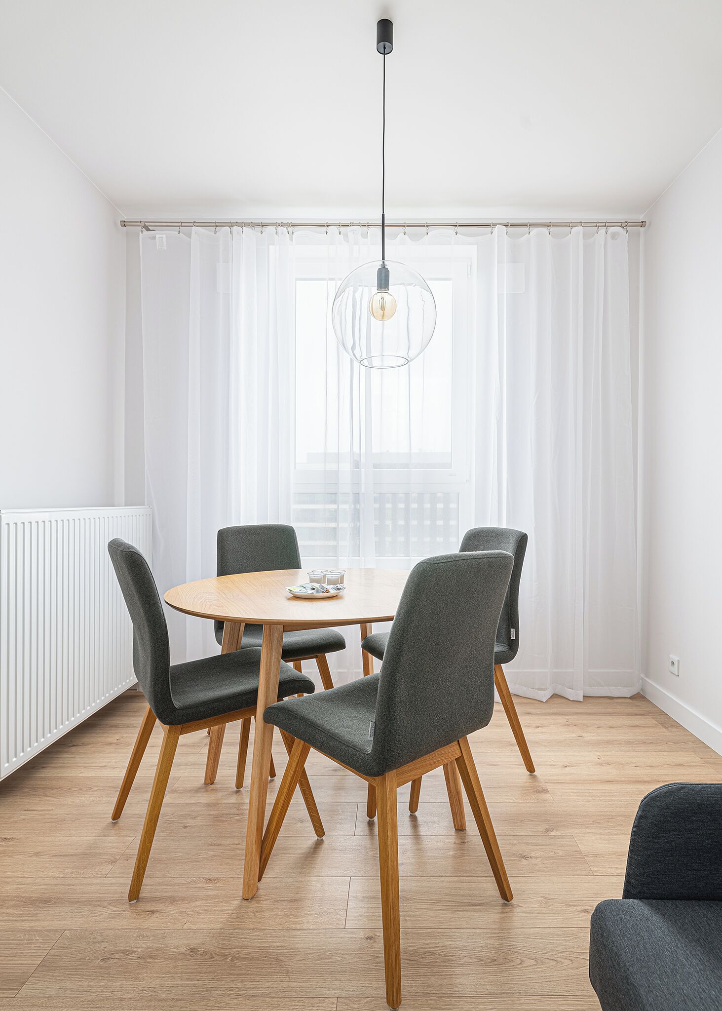 Un comedor moderno con una mesa redonda, cuatro sillas tapizadas en gris y una lámpara colgante.