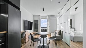 A modern hotel room with a kitchen area, a dining table with chairs, a sofa, and a bed. - RentPlanet - Apartamenty Wiktoryn (Warsaw)