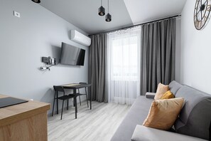 A modern living room with a grey sofa, a wooden desk, and a TV mounted on the wall.