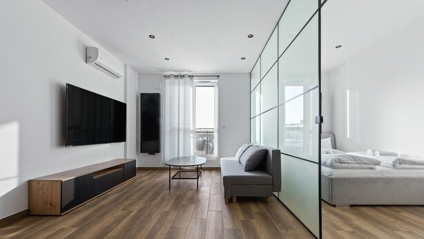 A modern living room with a flat-screen TV, a sofa, a dining table, and a bed. - RentPlanet - Apartamenty Wiktoryn (Warsaw)