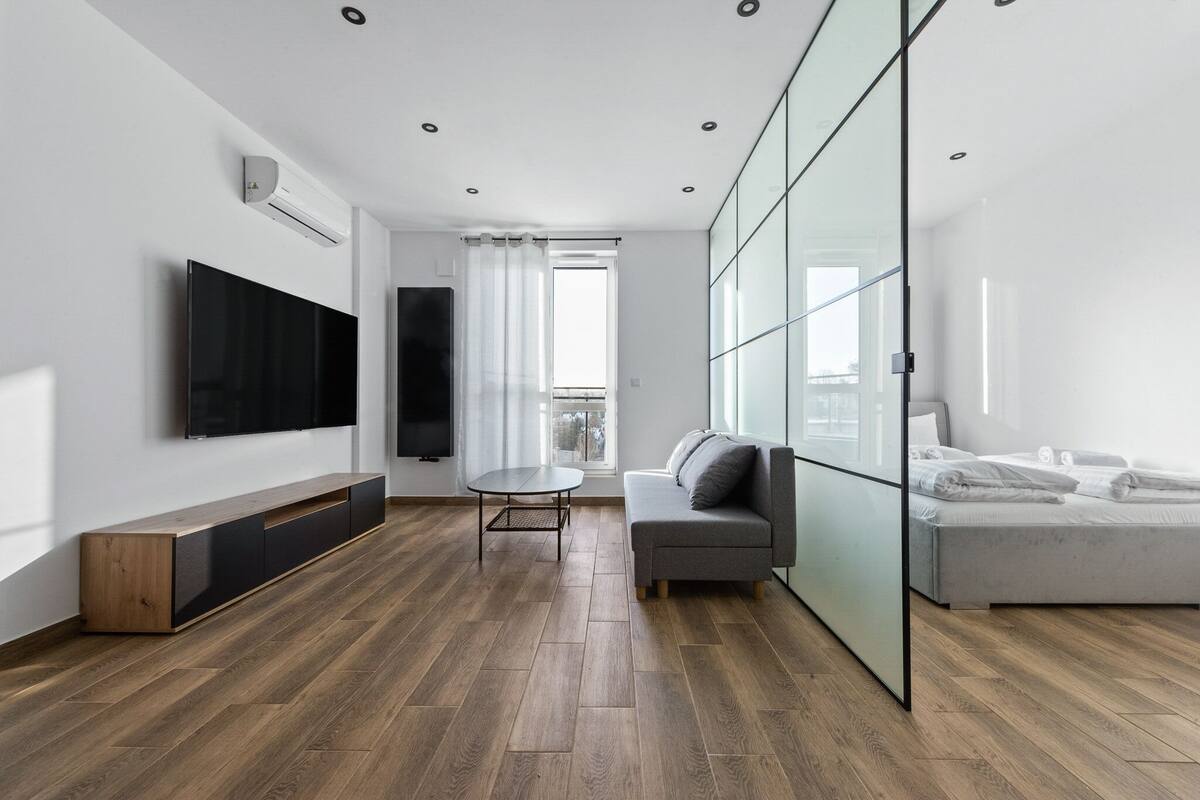 A modern living room with a flat-screen TV, a sofa, a dining table, and a bed.