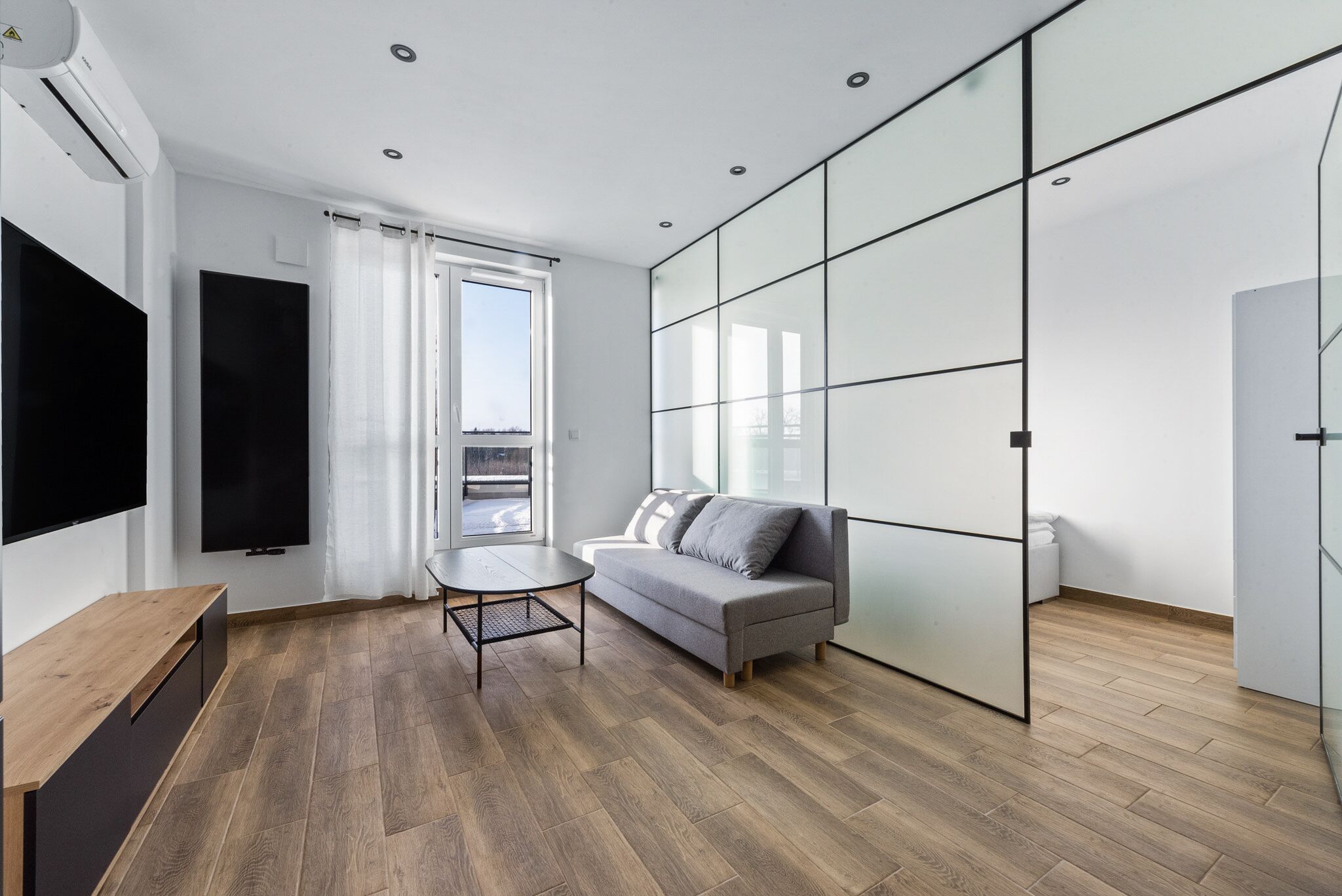 Een moderne woonkamer met een bank, een televisie, een tafel en een schuifpui naar buiten.