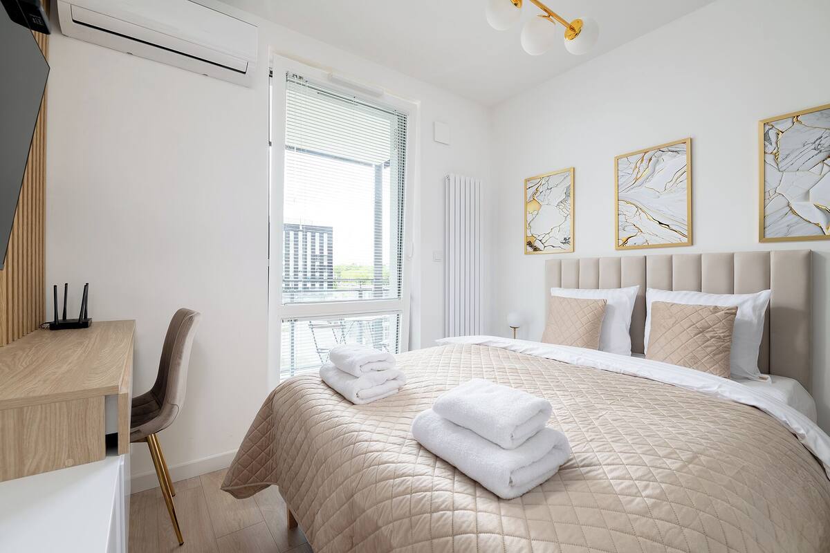 A hotel room with a bed, a desk, and a chair. There are three paintings on the wall.
