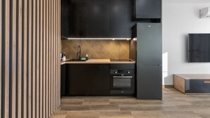 A modern kitchen with dark cabinetry, a herringbone-patterned backsplash, and built-in appliances. - RentPlanet - Apartamenty Wiktoryn (Warsaw)