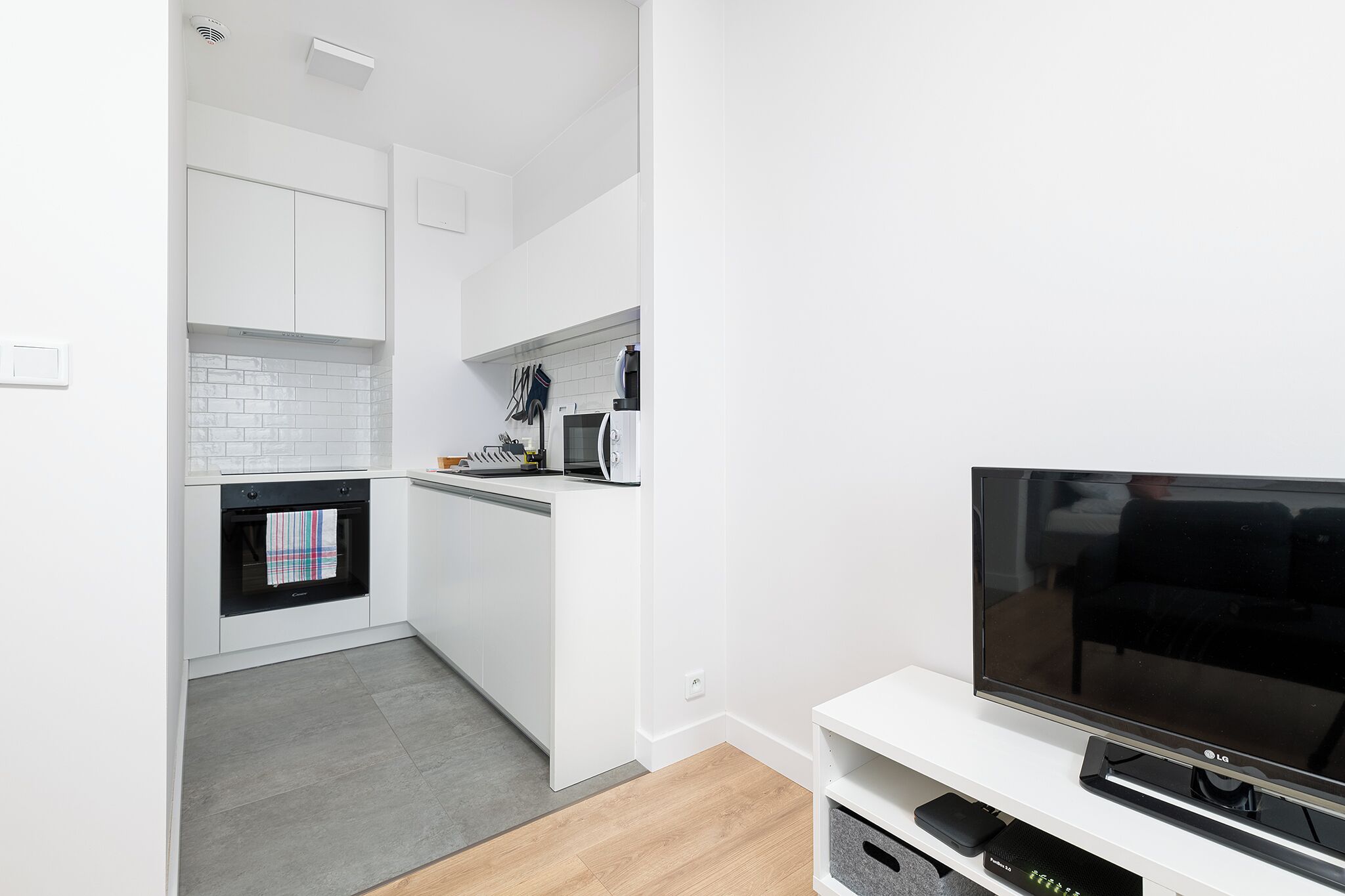 Uma cozinha moderna com armários brancos, micro-ondas e forno. Há uma televisão de tela plana em um suporte branco.