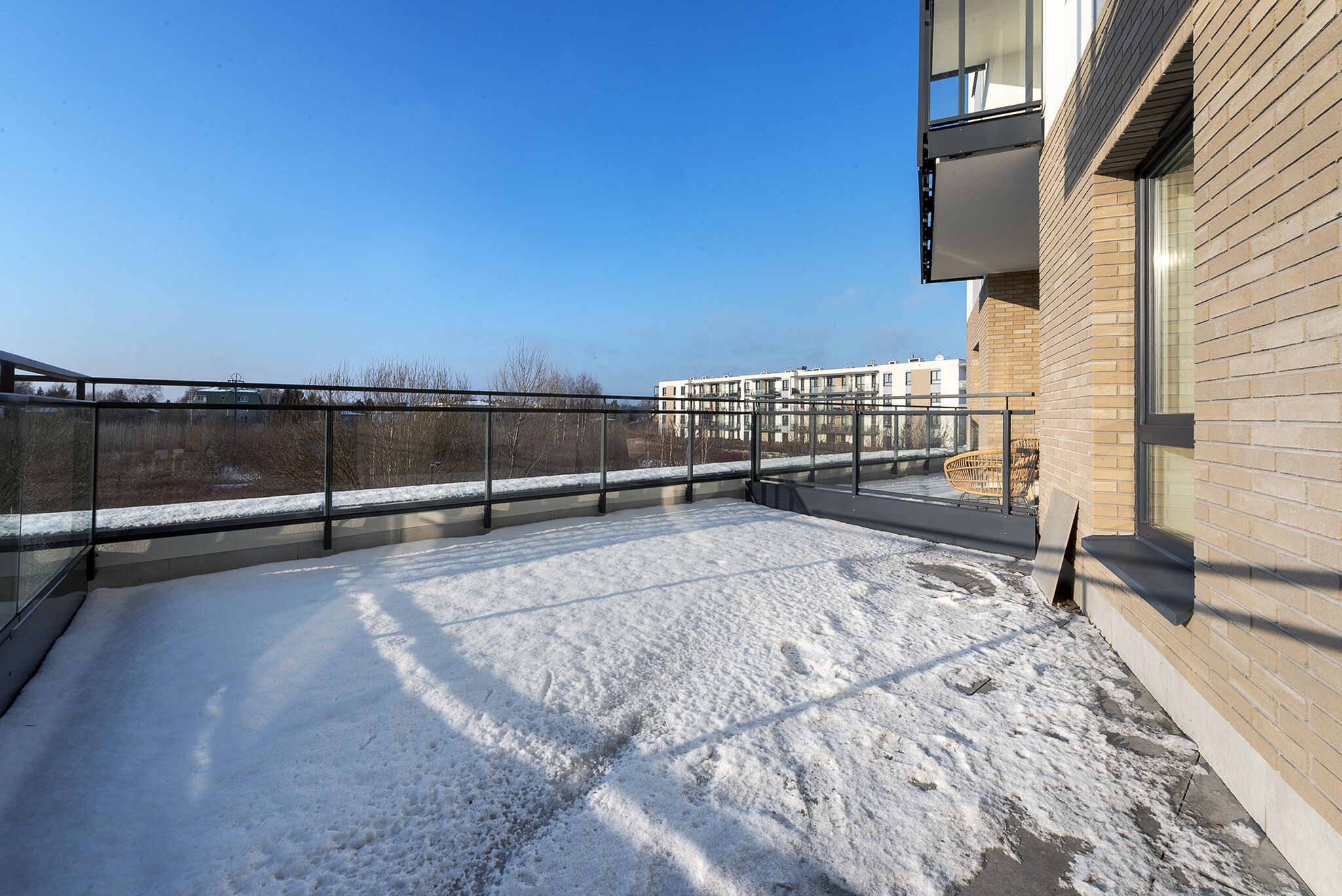 A rooftop terrace with a snow-covered ground, a glass balustrade, and a view of a distant building.