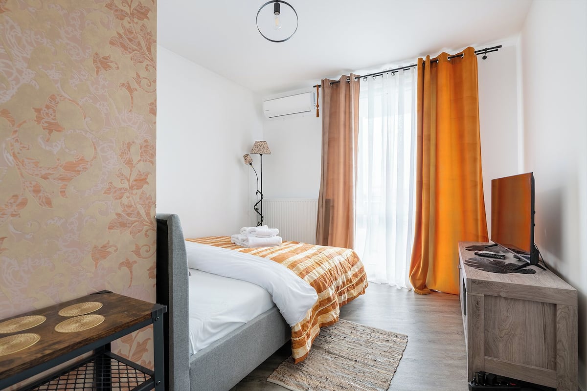 A bedroom with a bed, a bedside table, a lamp, and a TV stand.