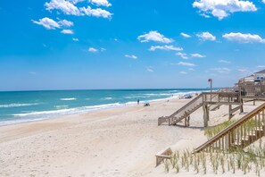 Une plage avec une promenade en bois, une jetée visible au loin et un ciel dégagé.