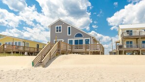 A beachfront house with a wooden staircase leading to a deck, surrounded by sand and under a partly cloudy sky. - Sea Glass - Fantastic Views from this 3 BR Oceanfront Home! (Surf City)