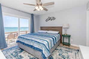 A bedroom with a bed, a ceiling fan, a nightstand with a lamp, a view of the ocean, and a decorative wall piece. - Sea Glass - Fantastic Views from this 3 BR Oceanfront Home! (Surf City)