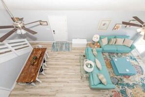 Un salon avec une table à manger en bois, un canapé de couleur turquoise et un ventilateur de plafond.