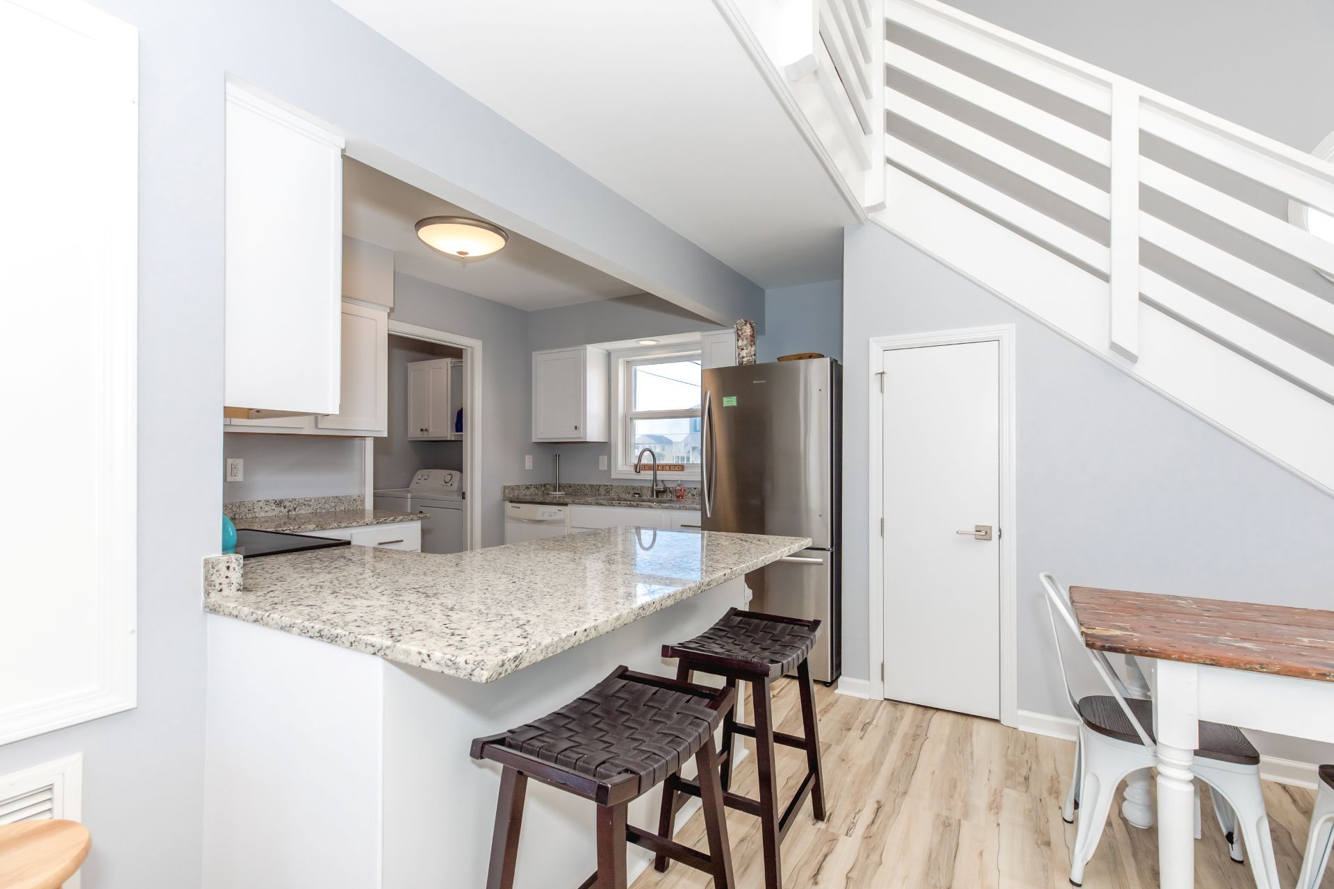 A modern kitchen with granite countertops, a stainless steel refrigerator, and a wooden dining table with bar stools.