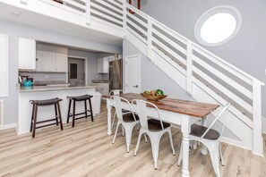 A modern kitchen with white cabinetry, a wooden dining table, and bar stools. - Sea Glass - Fantastic Views from this 3 BR Oceanfront Home! (Surf City)