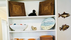 Un mueble blanco con estantes que contienen diverso menaje de cocina, un plato decorativo y cuadros de pared.