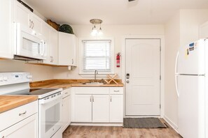 A compact kitchen with white cabinetry, a built-in oven, a microwave, a sink with a wooden countertop, and a refrigerator. - Beach Barn - Nice 5BR Oceanfront Home in Heart of Surf City (Surf City)