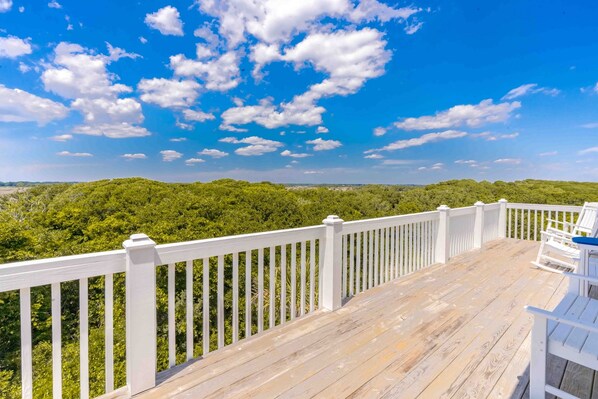 Une terrasse en bois avec des rampes blanches donnant sur un paysage boisé.