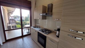 Une cuisine moderne équipée d’une cuisinière à gaz, d’un four et offrant une vue sur un balcon aménagé avec du mobilier d’extérieur.