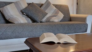 Un salon avec un canapé, des coussins à motifs, une table basse sur laquelle est posé un livre ouvert, un lampadaire et un tableau accroché au mur.