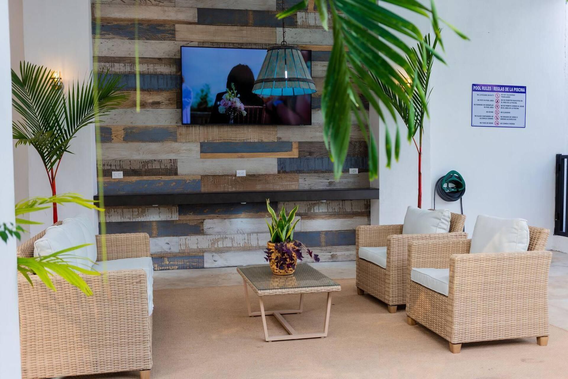 Een gezellige zithoek met rieten meubels, een flatscreen televisie aan een houten wand en een bord met regels voor het zwembad.