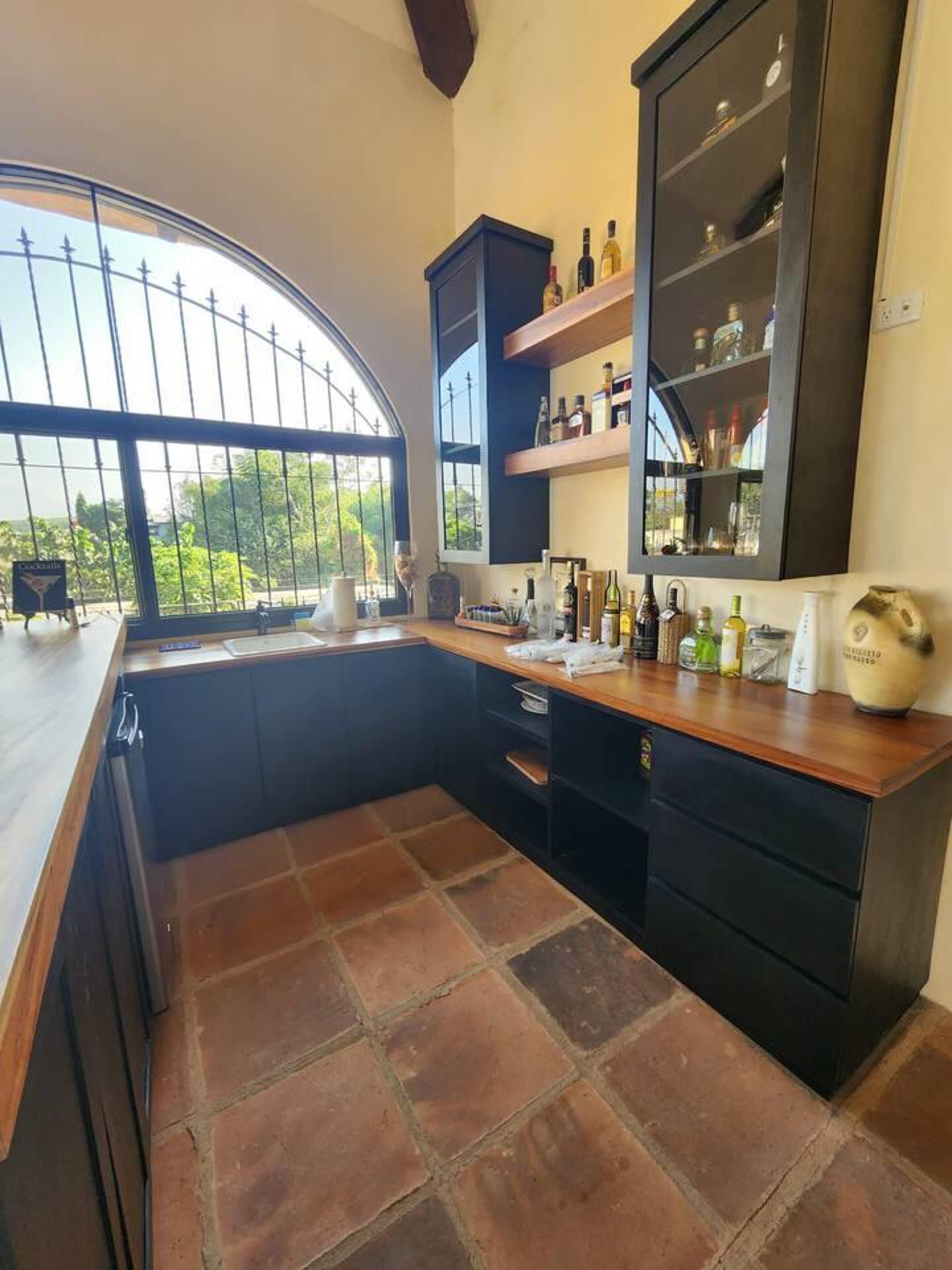 Una cocina con un gran ventanal, muebles oscuros y suelo de baldosas.