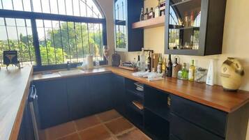 Una cocina con un gran ventanal, muebles oscuros y suelo de baldosas.