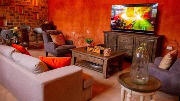 A cozy living room with a sofa, armchairs, a coffee table, and a television displaying a concert.