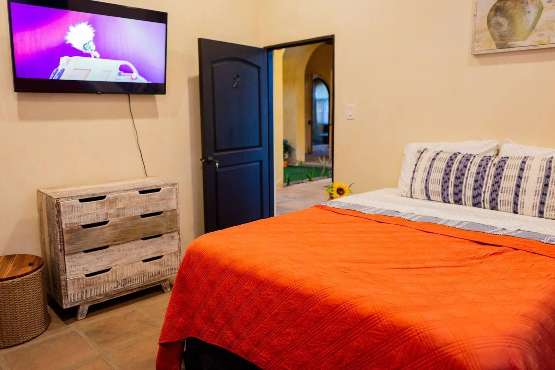 A bedroom with a bed, a television, a wooden chest, and a door leading to another room.