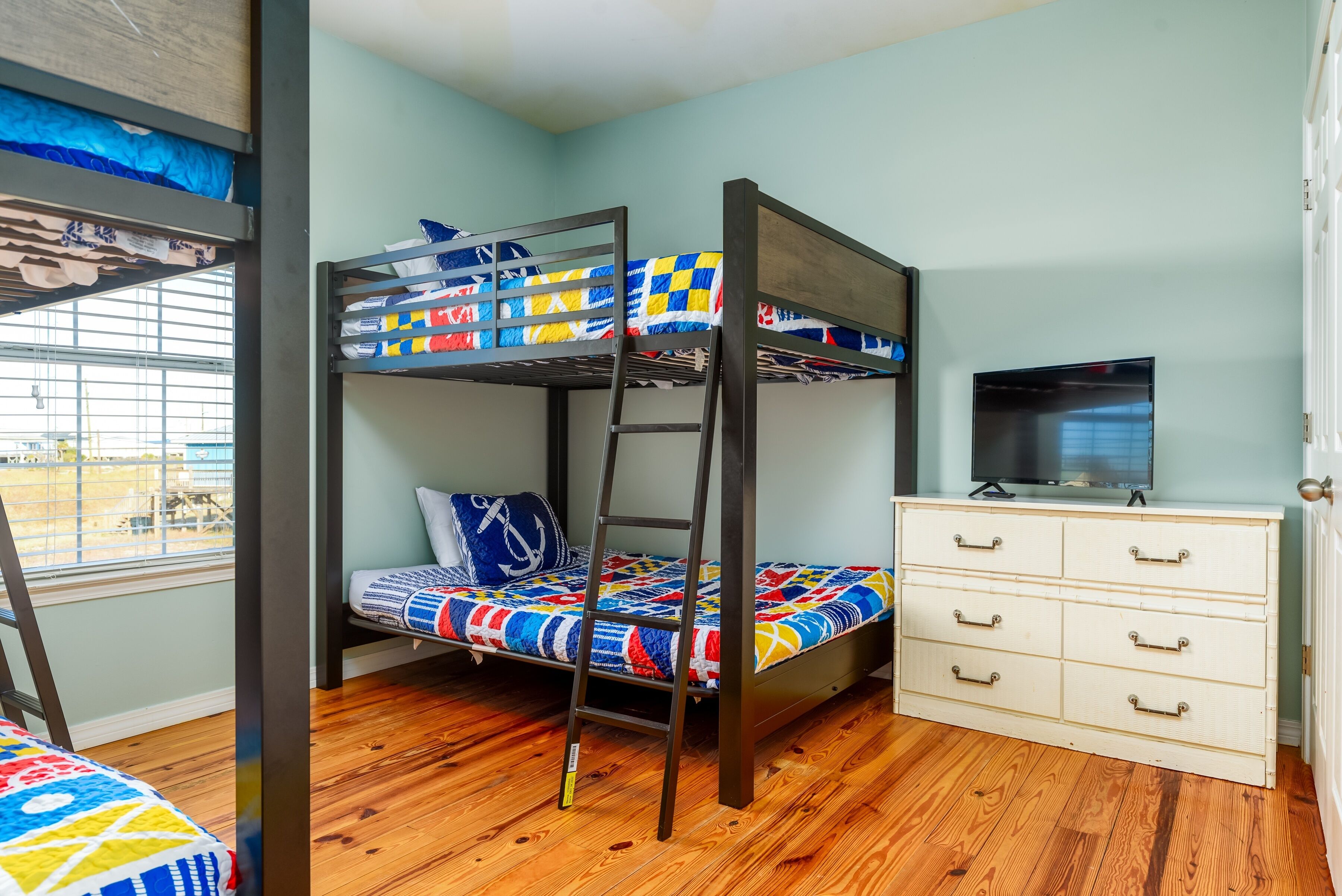 Una cama litera con escalera, un aparador con cajones y un televisor sobre un mueble.
