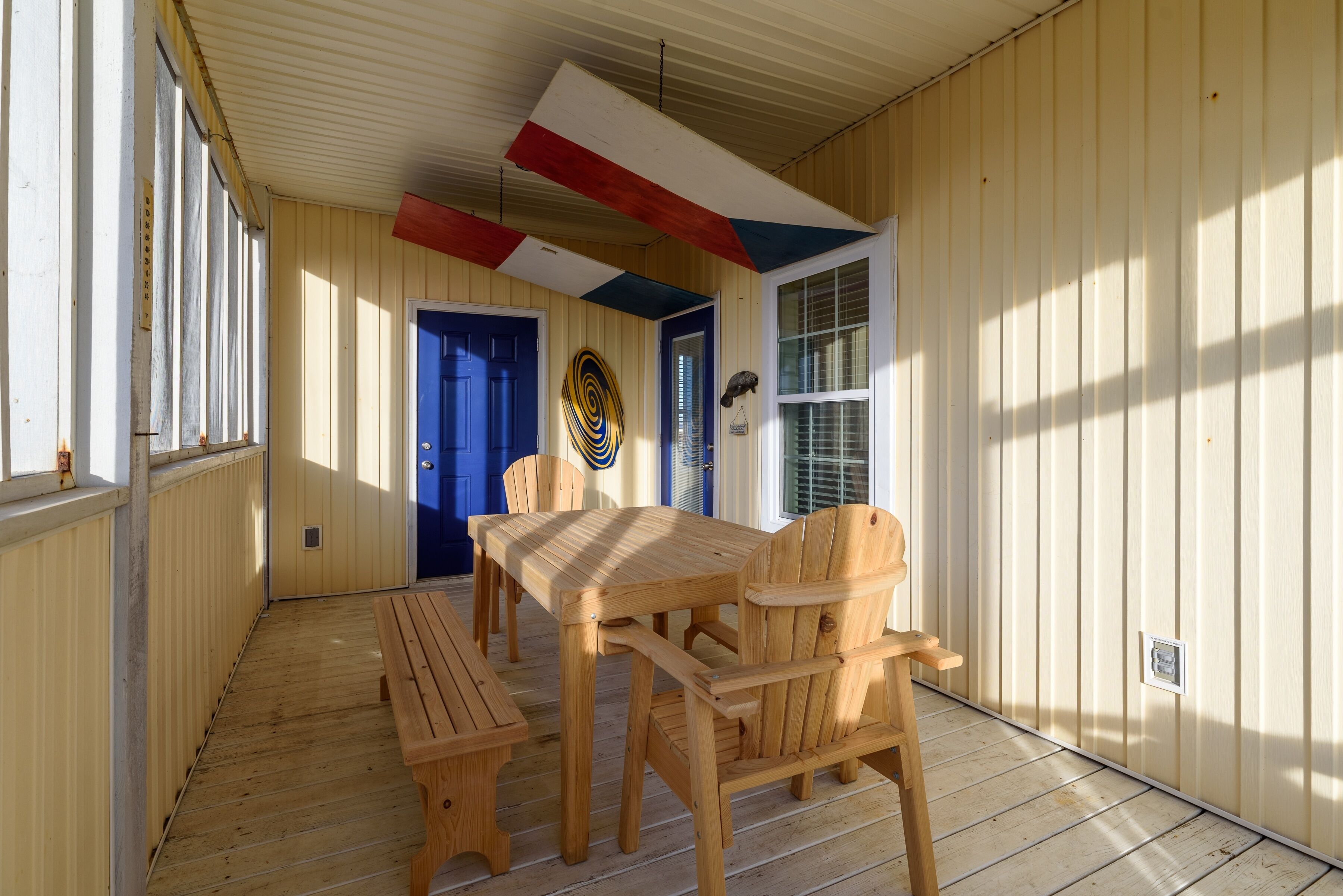 A covered porch with a wooden table and chairs, a blue door, and a window with blinds.