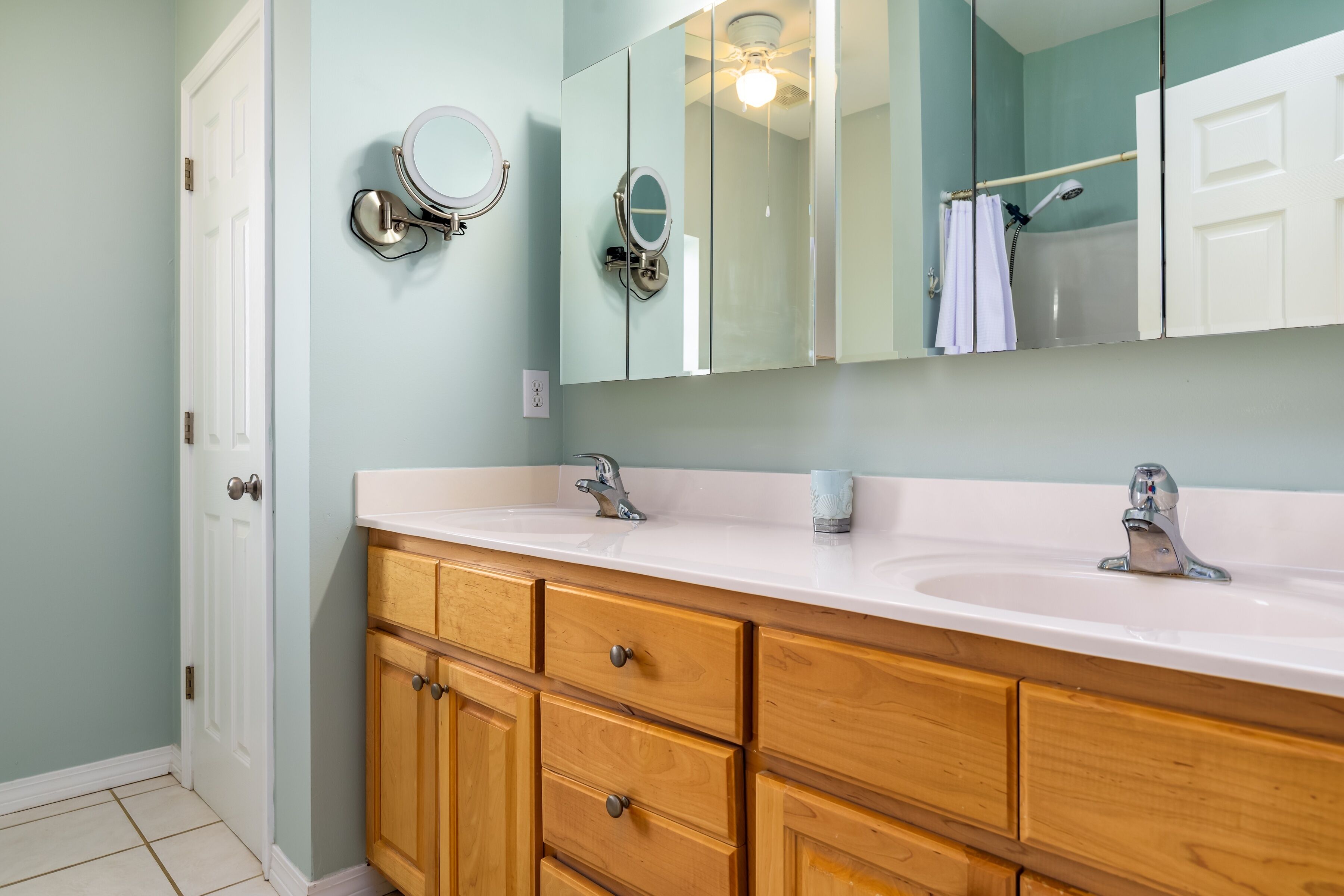 A bathroom with two sinks, wooden cabinets, a large mirror, and a shower area.