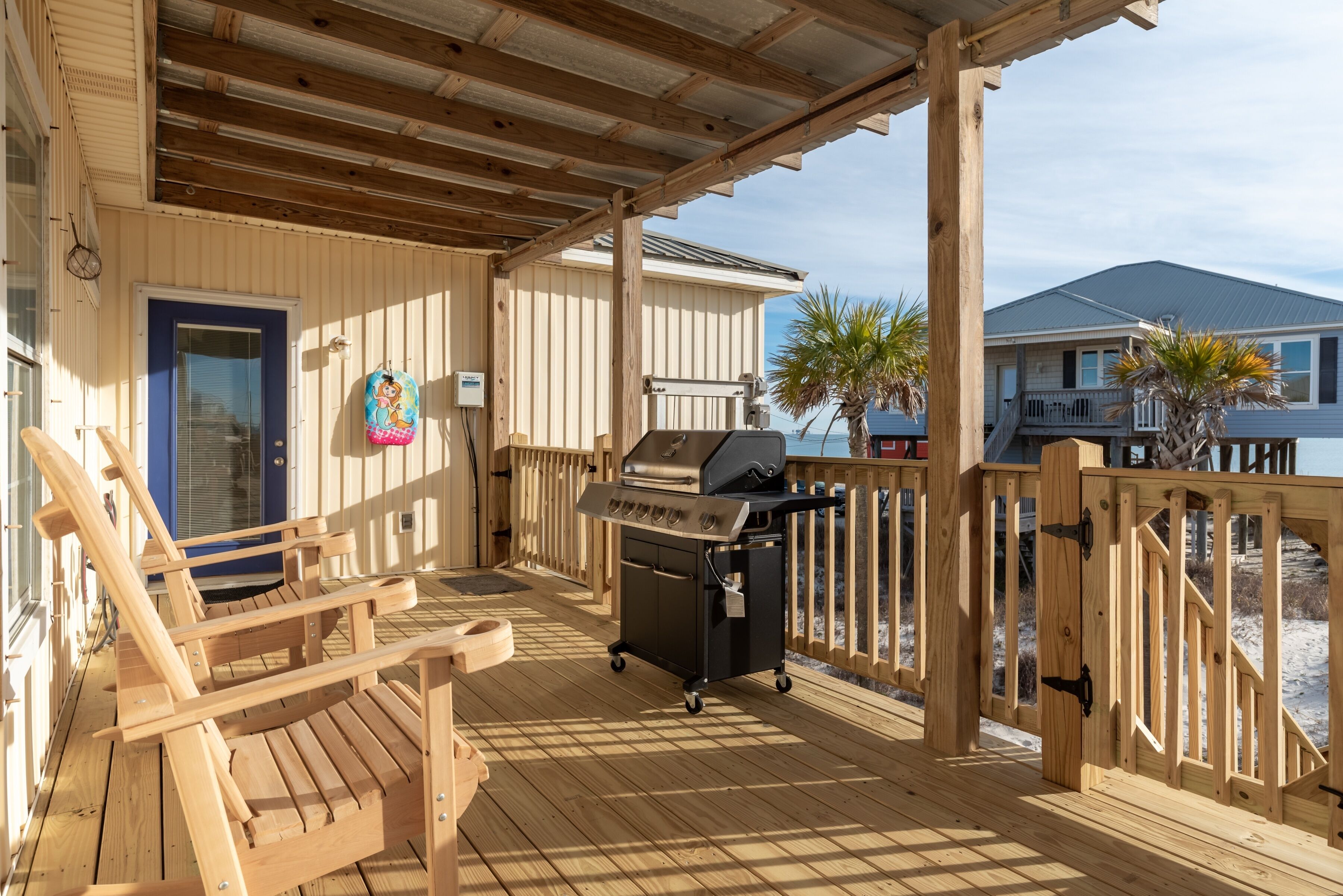 A wooden deck with a grill, a blue door, and a wooden chair.