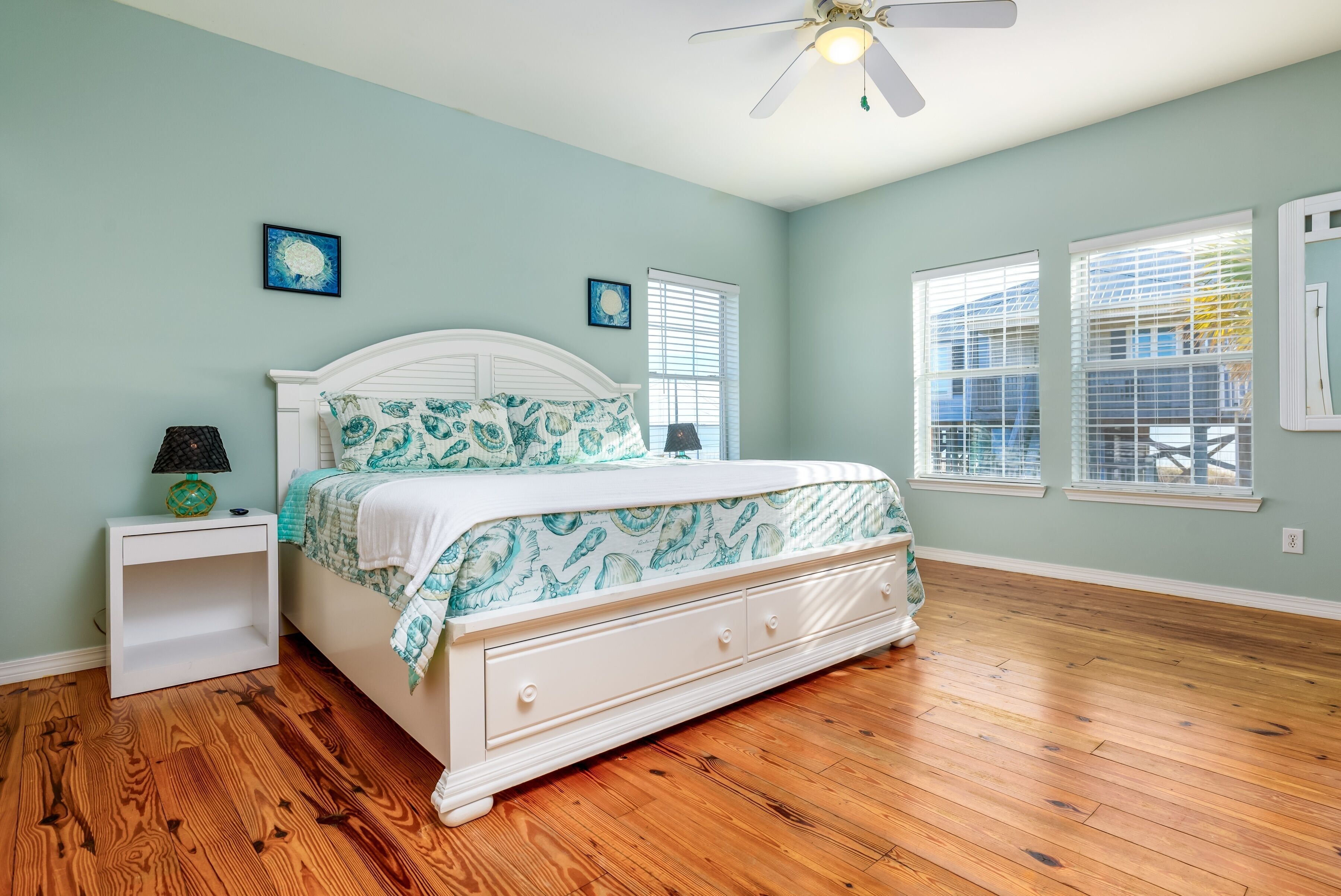 Un dormitorio con cama blanca, suelo de madera y ventilador de techo.