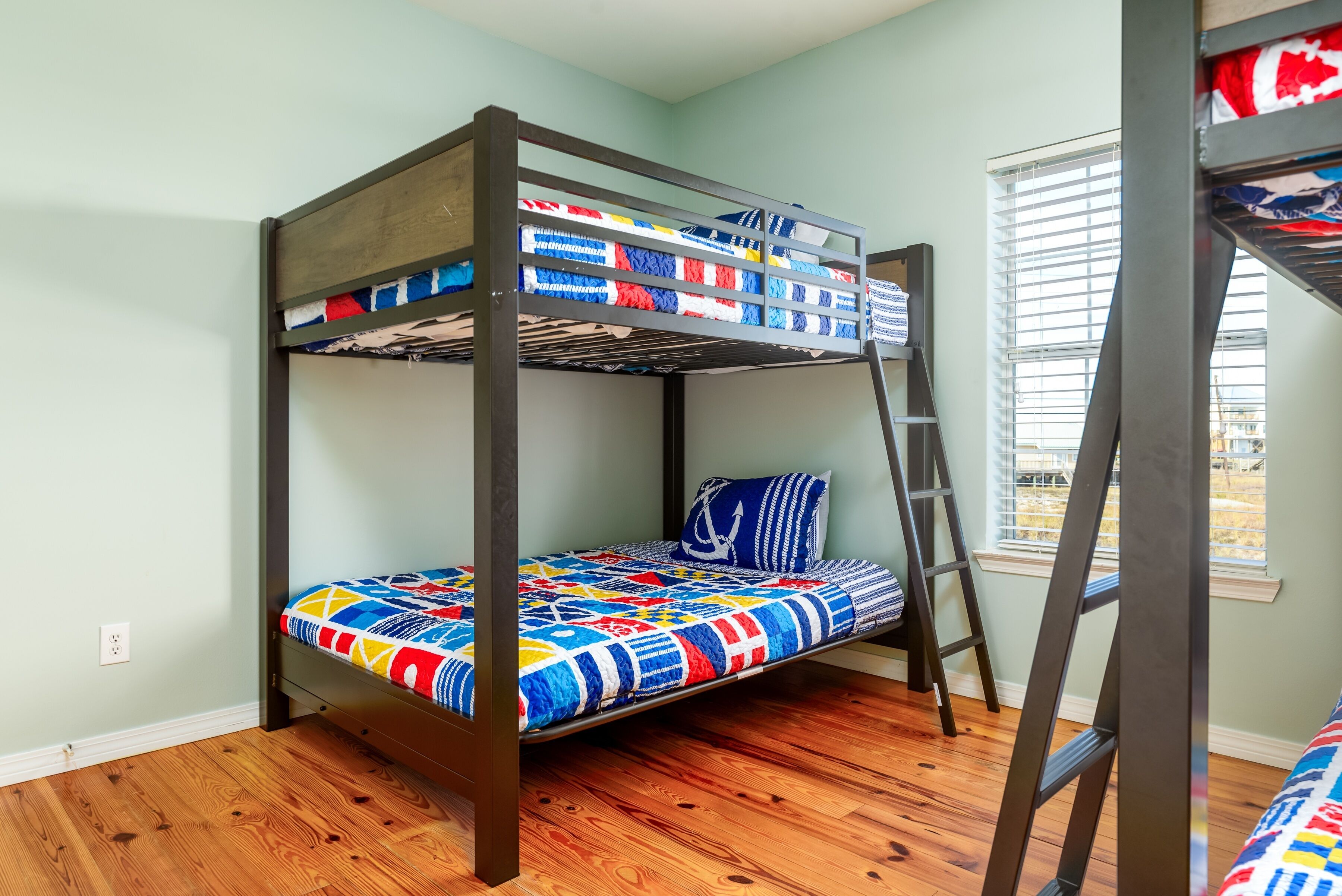 Una cama litera con un edredón colorido, piso de madera y una ventana con persianas.
