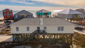 A coastal building with a metal roof, a blue door, and a staircase leading to a deck. - Coconut Breeze - 105 St Dennis 4 Bedroom Home by RedAwning (Dauphin Island)