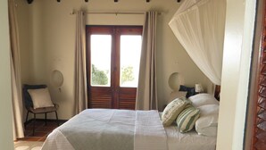 A bedroom with a bed, curtains, a chair, a ceiling fan, and a view through a door. - Calypso Court - Private 1 bedroom villa with pool 1 Villa by RedAwning (Gros Islet)