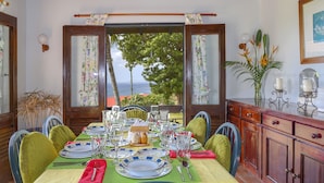 A dining table set with plates, glasses, and cutlery, with a view of the sea through open windows. - Calypso Court - Private 1 bedroom villa with pool 1 Villa by RedAwning (Gros Islet)