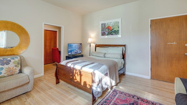 A bedroom with a wooden bed, a round mirror, a television, and a door. - Downtown Oakland Studio, 6 Mi to Toll Plaza Beach! (Oakland)