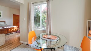 A room with a glass table, orange chairs, a wooden bed, and a window with curtains. - Downtown Oakland Studio, 6 Mi to Toll Plaza Beach! (Oakland)