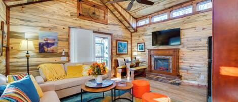 Interior acogedor de una cabaña con techo de madera, chimenea, sofá, mesa de comedor y televisor.